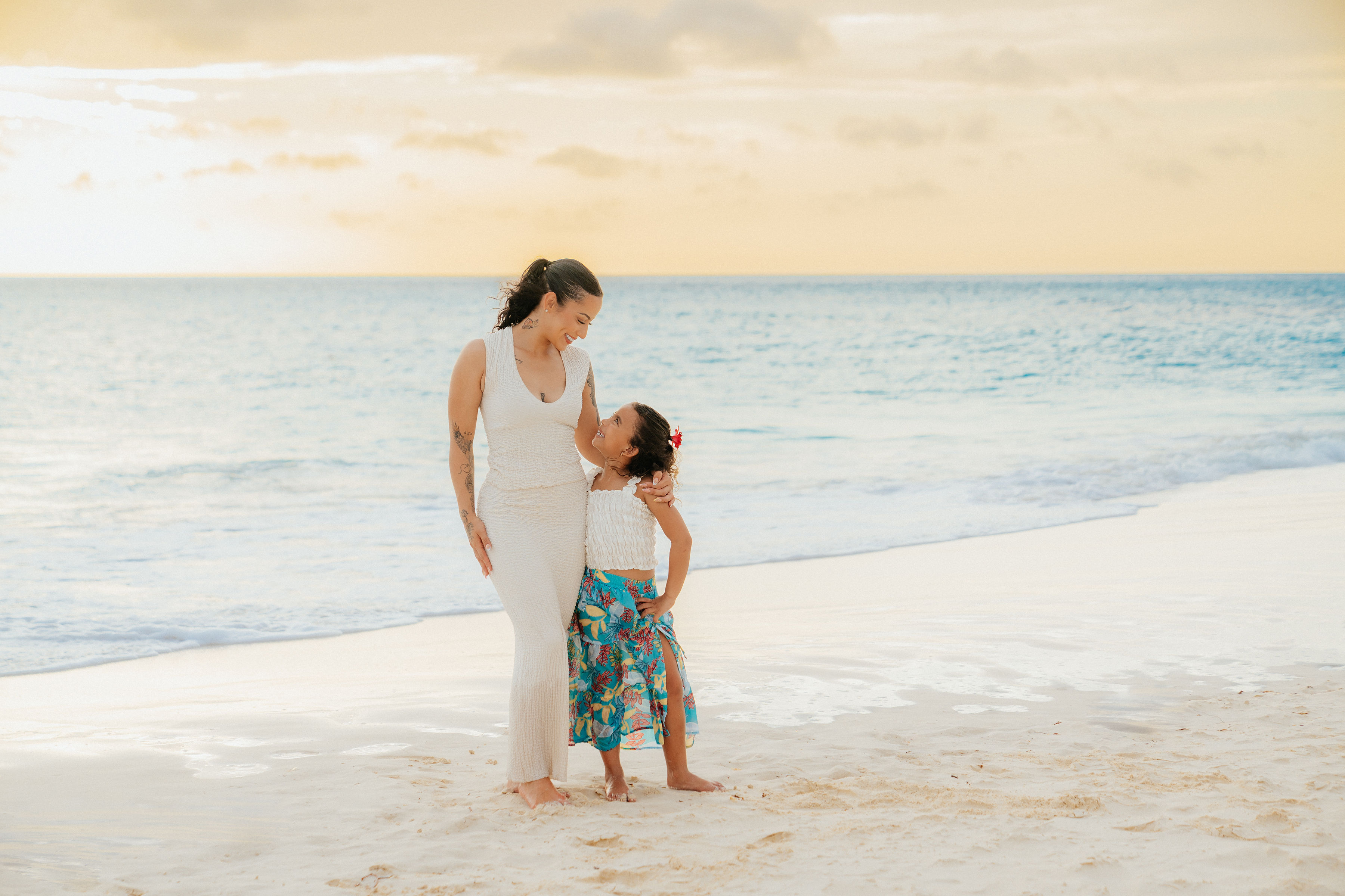 Naomi, oprichter van Tiny Travelers Aruba, staand met haar arm om haar dochter heen op een strand op Aruba bij zonsondergang