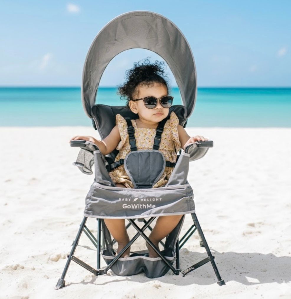 Toddler in sunglasses seated in a GoWithMe canopy beach chair by turquoise water