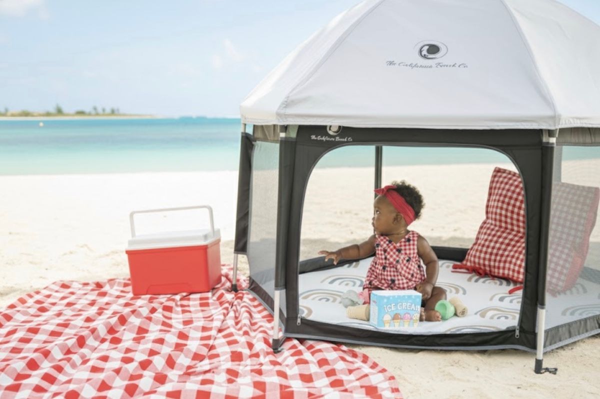 Baby sitting inside a California Beach Co. POP N' GO tent on a white-sand beach